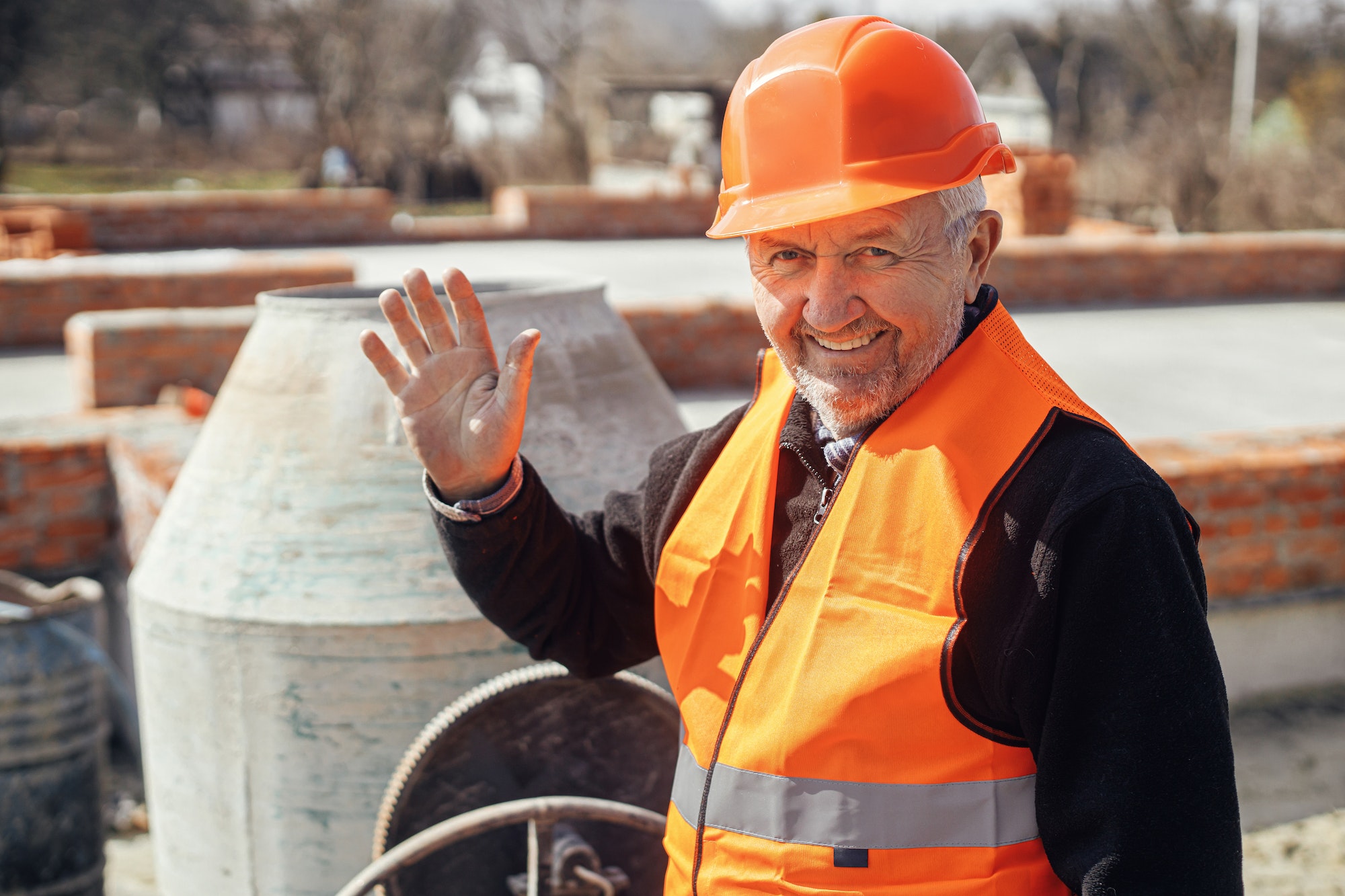 Happy senior foreman in hard hat standing on background of construction site